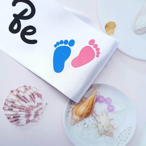 Macro shot of white satin Mommy to Be sash with blue and pink baby footprints