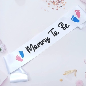 Detail of white satin Mommy To Be sash with gold lettering and cute baby footprints