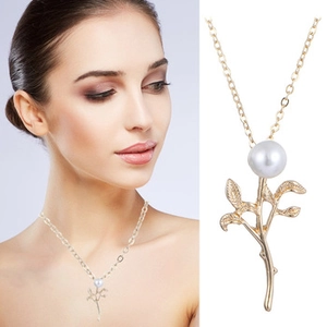 Detail view of a gold leaf branch necklace featuring a white pearl on a delicate chain