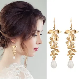 Detail of golden leaf dangle earrings with white teardrop pearls shown on model