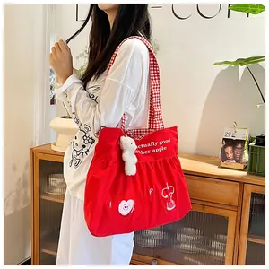 Detail of a red large-capacity canvas bag featuring apple print and a cute bear pendant
