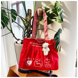 Detail of red nylon tote bag with apple prints and check pattern shoulder strap