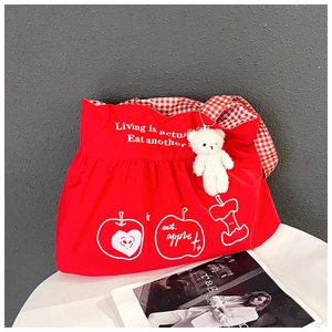 Detailed shot of red nylon tote bag with apple print, checkered straps and plush bear charm