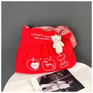 Detail of red travel bag featuring white apple graphics and a plush bear keychain