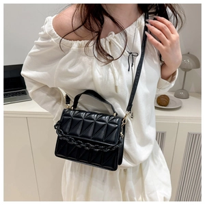 Detail of black quilted crossbody bag with chunky acrylic chain in home office setting