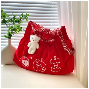 Detail of red nylon tote bag with plaid shoulder strap and plush bear charm