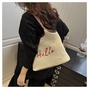 Close-up of woven straw tote bag with red Hello embroidery and brown leather straps