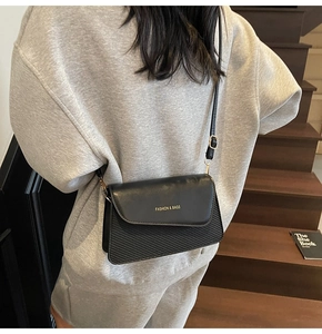 Detailed view of black crossbody bag with diagonal textures and gold buckle on a model