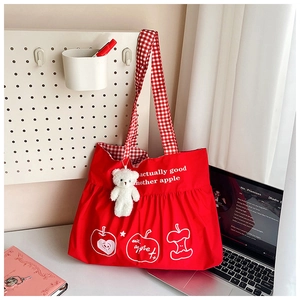 Detail of red nylon tote with plaid straps and cute plush bear charm in a desk setting
