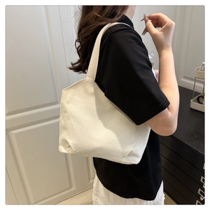 Minimalist off-white canvas tote bag shown as a shoulder bag on a female model