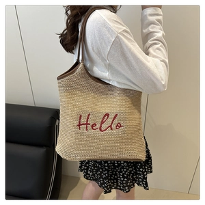 Detail of handwoven straw tote bag with red Hello embroidery and brown leather strap