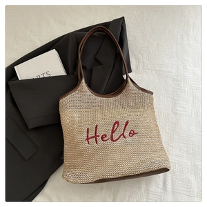 Detail of beige woven tote bag with red Hello embroidery and brown leather handles