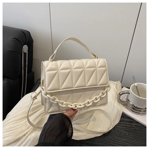 Detailed view of quilted beige handbag with acrylic chain and textured leather on fabric
