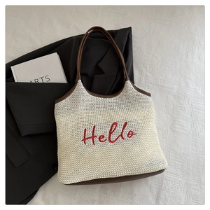 Detail of Hello embroidery and brown leather handles on a cream woven tote bag