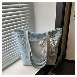 Close-up of light blue quilted tote bag with silk scarf on handle and bow pattern