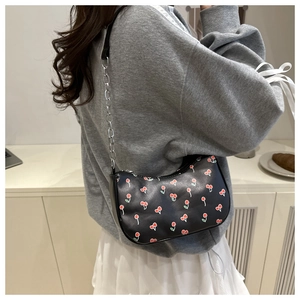 Detail of black underarm bag with cherry print and silver chain strap on model