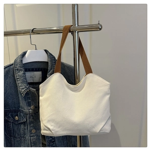 Detail of white canvas tote bag with brown woven handles hanging on a metal rack