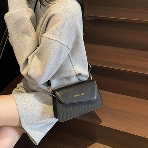 Minimalist black crossbody bag with letter print and leather texture on a wooden staircase