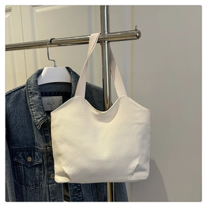 Detailed view of a white canvas tote bag with wide shoulder straps on a metal hanger