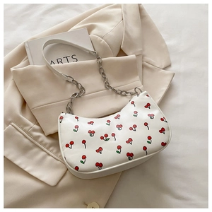 Detail of cherry print shoulder bag featuring metal chain strap on beige blazer