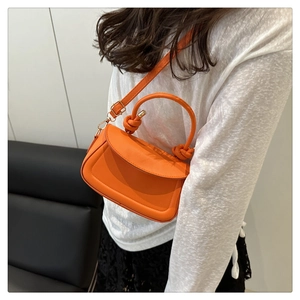 Detail of a bright orange crossbody bag with knot handle and adjustable strap worn on person