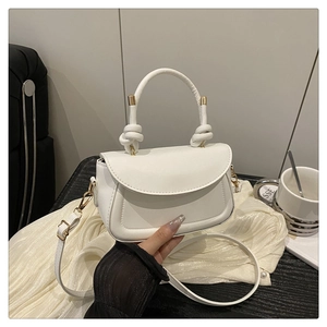 Close-up of a white leather crossbody bag with knot handle and gold hardware on fabric
