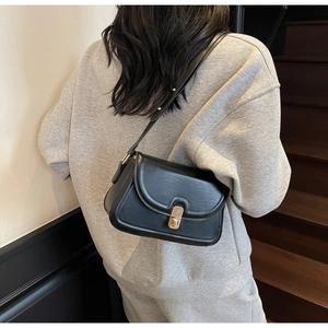 Détail d'un sac bandoulière en cuir noir avec fermoir doré sur un sweat gris