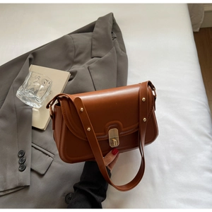 Détail d'un sac bandoulière en cuir marron vintage avec fermoir en métal sur costume