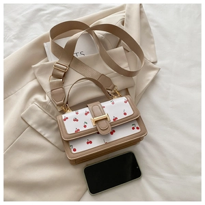 Détail d'un sac à bandoulière crème avec imprimés cerises et large sangle textile