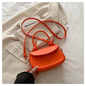 Detail of orange leather crossbody bag with knot handle and curved silhouette