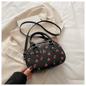 Detailansicht einer schwarzen Boston Bag mit Kirschprint auf einem beigen Blazer