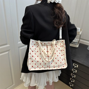 Cream corduroy tote bag with red heart pattern and dual handles shown in a lifestyle setting