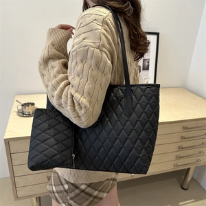 Ensemble sac cabas noir matelassé et pochette porté dans un décor d'intérieur