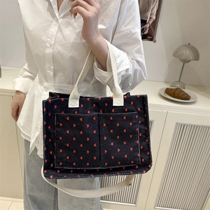 Large black corduroy tote bag with red hearts and white crossbody strap in lifestyle setting