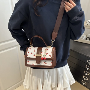 Chic women's crossbody bag with cherry print and contrast trim in natural indoor lighting