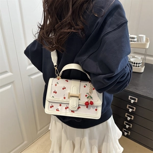 Sac bandoulière blanc à motif cerises rouges et fermoir doré porté par un modèle