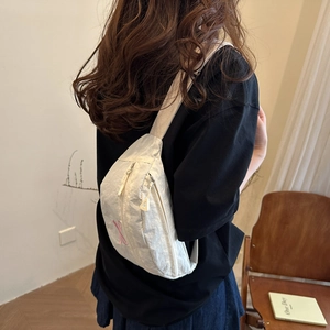 White pleated nylon chest bag with pink embroidery worn by a model in a cozy indoor setting