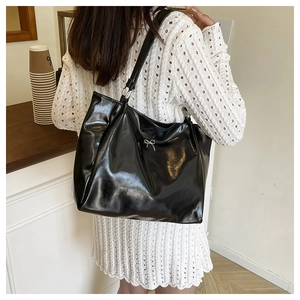Detail of glossy black tote bag featuring a silver bow accent and leather strap