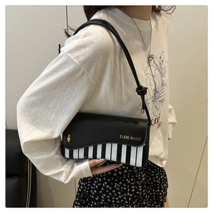 Close-up of piano key pattern and gold music slogan on a black crossbody bag