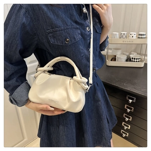 Detail of a creamy beige pleated handbag with a knotted handle and embossed logo text