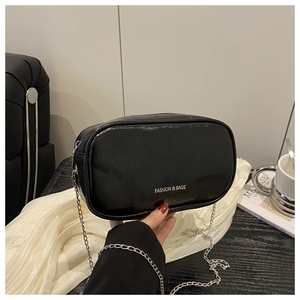 Détail du sac polochon en cuir verni noir avec chaîne argentée et logo texte tendance