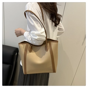 Rear side view of a large beige PU leather tote bag with brown trim on a female model