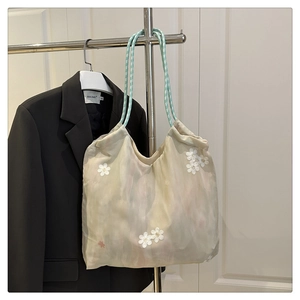 Detail of canvas tote bag featuring white daisy embroidery and mint green braided rope straps