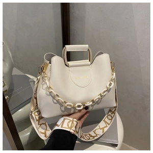 Detail of off-white bucket bag featuring metal chain decor and a wide patterned strap