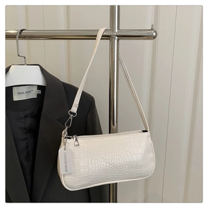 Detail of white crocodile embossed baguette bag with silver hardware on suit background