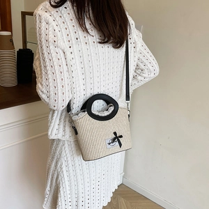 Beige woven bucket bag with lace trim and black bow detail shown on a model