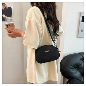 Detailed side view of a minimalist black nylon crossbody bag on a model with adjustable strap