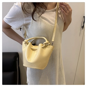 Detail of light yellow glossy bucket bag with knotted handle and fashion branding