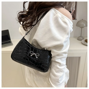 Detail of black faux crocodile leather shoulder bag with a silver metal bow buckle