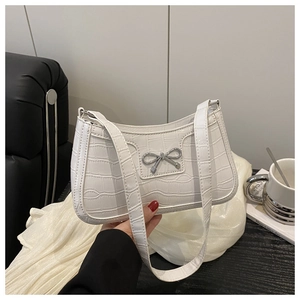 Detail of white crocodile texture underarm bag with silver metal bow and shoulder strap